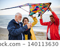Grandparents with preteen girl preparing kite for flying on sandy beach. 140113630