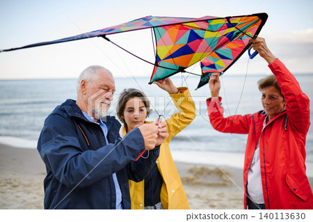 Grandparents with preteen girl preparing kite for flying on sandy beach. Grandparents with preteen girl preparing kite for flying on sandy beach. 140113630