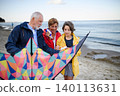 Grandparents with preteen girl preparing kite for flying on sandy beach. 140113631