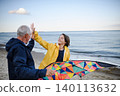 Senior man and his preteen granddaughter preparing kite for flying on sandy beach. 140113632