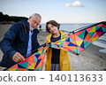Senior man and his preteen granddaughter preparing kite for flying on sandy beach. 140113633