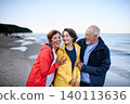 Grandparents walking with teenage granddaughter on beach during family vacation. 140113636