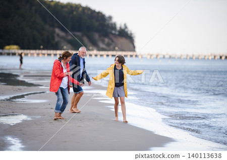 Grandparents walking with teenage granddaughter on beach during family vacation. 140113638