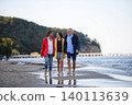 Senior couple holding hands with their preteen granddaughter and walking on sandy beach. 140113639