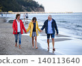 Senior couple holding hands with their preteen granddaughter and walking on sandy beach. 140113640
