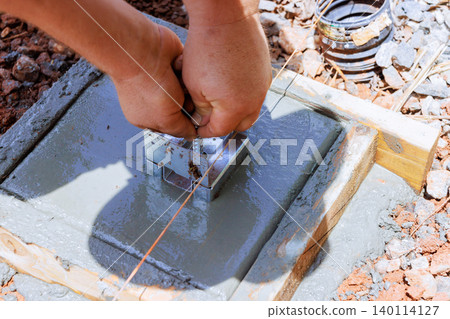 Construction worker secures metal anchor in fresh concrete at building site. Construction worker secures metal anchor in fresh concrete at building site. 140114127