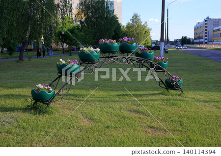 Wrought iron flower arch with green petunia pots on lawn grass, urban street landscape design element Wrought iron flower arch with green petunia pots on lawn grass, urban street landscape design element 140114394