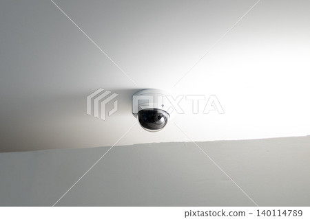 Dome security camera mounted on white ceiling with bright light reflection Dome security camera mounted on white ceiling with bright light reflection 140114789