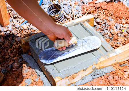 Worker levels fresh concrete with trowel on wooden frame at construction site Worker levels fresh concrete with trowel on wooden frame at construction site 140115124