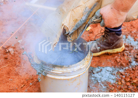 Someone pours dry mixture into bucket at construction site while smoke comes out dust is present on ground. Someone pours dry mixture into bucket at construction site while smoke comes out dust is present on ground. 140115127