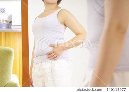一位女士對著鏡子,擔心自己隆起的肚子。 一位女士對著鏡子,擔心自己隆起的肚子。 140115977