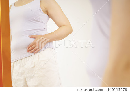 A woman is worried about her protruding belly in front of the mirror. A woman is worried about her protruding belly in front of the mirror. 140115978