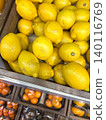 Colorful yellow lemons CITRUS LIMON and some tangerines blurred, on the counter of a fruit and vegetable shop in wooden box, close-up 140116769