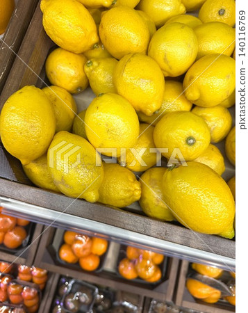 Colorful yellow lemons CITRUS LIMON and some tangerines blurred, on the counter of a fruit and vegetable shop in wooden box, close-up 140116769