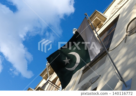 Pakistani flag swaying in the wind against blue sky and historical buildings. Flag of Pakistan. Flag day celebration concept, patriotism concept. Embassies and consulates of countries 140116772