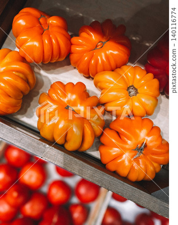 Colorful tomatoes ACCORDION ORANGE and some red tomatoes blurred, on the counter of a vegetable shop in wooden box, close-up. 140116774