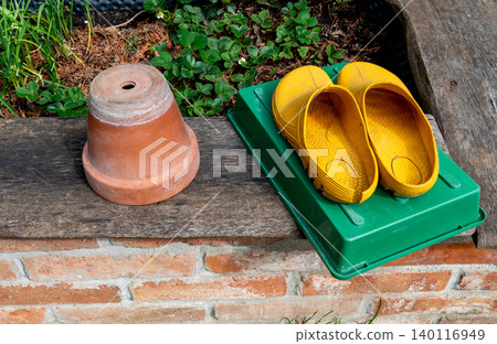 yellow Garden Clogs and Flower Pot on Raised Bed 140116949