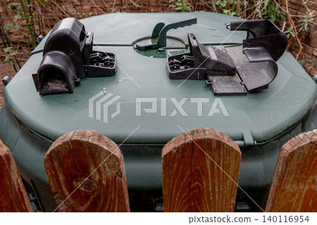 Outdoor compost bin with plastic rodent traps behind wooden fence Outdoor compost bin with plastic rodent traps behind wooden fence 140116954