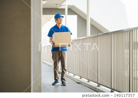 A delivery man carrying a package into an apartment building. A delivery man carrying a package into an apartment building. 140117357