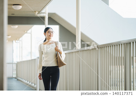 一位年輕女子正走在公寓大樓的走廊上準備出門。 一位年輕女子正走在公寓大樓的走廊上準備出門。 140117371