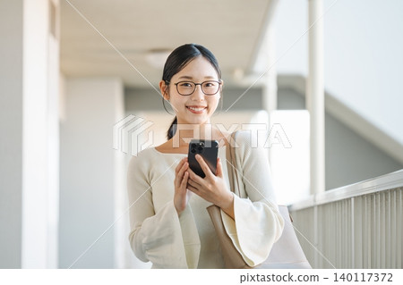 一位年輕女子在公寓大樓的走廊上拿著她的智慧型手機。 140117372