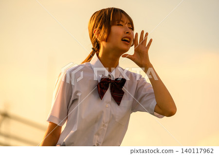 A high school girl shouting towards the setting sun 140117962