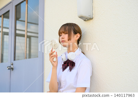 High school girl cooling off with a fan High school girl cooling off with a fan 140117963