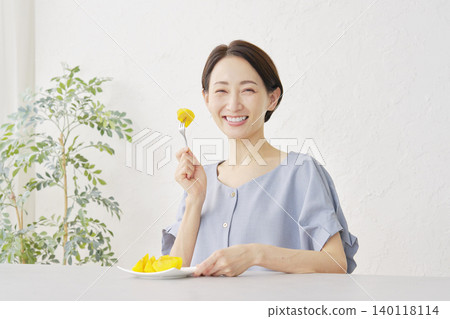 Woman eating persimmon in the living room, looking at camera, portrait Woman eating persimmon in the living room, looking at camera, portrait 140118114