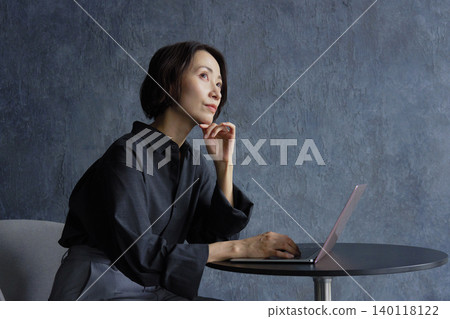 A businesswoman using a computer, thinking, against a black background. 140118122