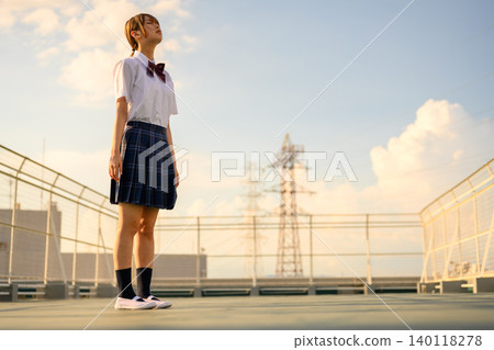 Schoolgirl looking up at the sky on the roof 140118278