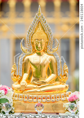 A golden Buddha statue sits in a peaceful meditation pose, decorated with sparkling crystal details. Soft temple architecture and floral offerings appear in the background. A golden Buddha statue sits in a peaceful meditation pose, decorated with sparkling crystal details. Soft temple architecture and floral offerings appear in the background. 140118604