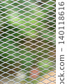 Metal mesh screen with diamond shaped openings. Silver grid pattern looks clean, modern, and strong, with soft green outdoor blur behind it. 140118616