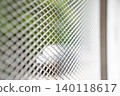 Metal mesh screen with diamond shaped openings. Silver grid pattern looks clean, modern, and strong, with soft green outdoor blur behind it. 140118617