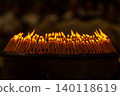 Close up rows of small burning candles capture soft smoke, flickering firelight, and an emotional low light moment of prayer and remembrance. 140118619