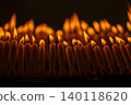Close up rows of small burning candles capture soft smoke, flickering firelight, and an emotional low light moment of prayer and remembrance. 140118620