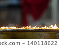 Close up rows of small burning candles capture soft smoke, flickering firelight, and an emotional low light moment of prayer and remembrance. 140118622
