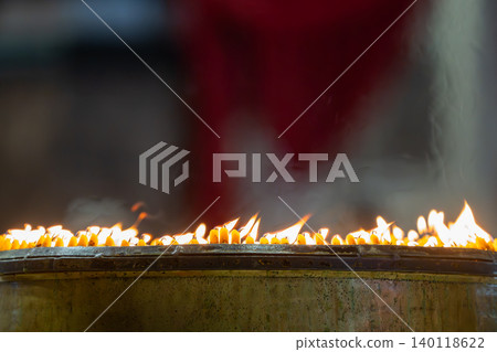 Close up rows of small burning candles capture soft smoke, flickering firelight, and an emotional low light moment of prayer and remembrance. 140118622