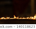 Close up rows of small burning candles capture soft smoke, flickering firelight, and an emotional low light moment of prayer and remembrance. 140118623