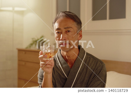 一位老年男子在臥室裡喝威士忌，肖像照，他正看著鏡頭。 140118729