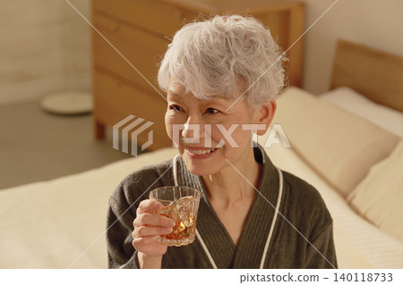 Senior woman drinking whiskey in bedroom 140118733