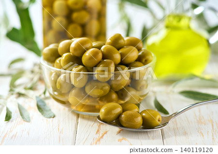 tasty green olives in a clear glass bowl on a white table. tasty green olives in a clear glass bowl on a white table. 140119120