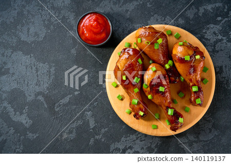 Fried chicken legs with sauce on a black table, top view. Roast chicken drumsticks with ketchup. Fried chicken legs with sauce on a black table, top view. Roast chicken drumsticks with ketchup. 140119137