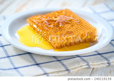 Sweet golden bee honey dripping out of honeycomb in a plate, selective focus. Sweet golden bee honey dripping out of honeycomb in a plate, selective focus. 140119139