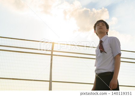 A boy in a school uniform looking up at the sky 140119351