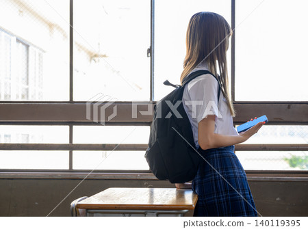 A high school girl holding her smartphone by the window. 140119395