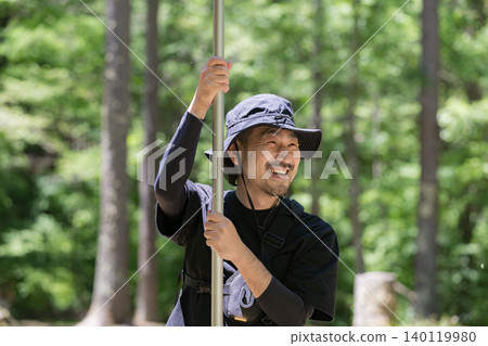 一名男子在森林裡搭建帳篷和防水布,享受戶外自然體驗的樂趣。 一名男子在森林裡搭建帳篷和防水布,享受戶外自然體驗的樂趣。 140119980