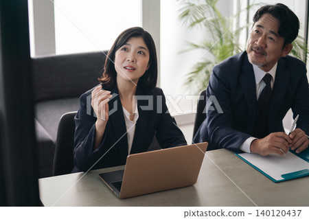 A group of business people conversing while looking at a screen. A group of business people conversing while looking at a screen. 140120437