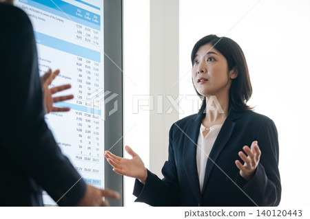 一群商務人士一邊看著螢幕一邊交談。 一群商務人士一邊看著螢幕一邊交談。 140120443
