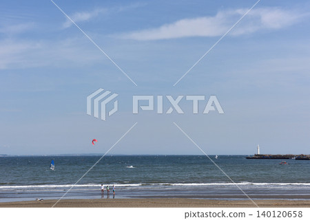 People playing at the water's edge of Katase Higashihama Beach under a clear blue sky. 140120658