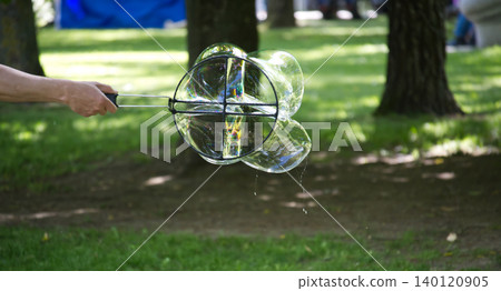 Hand holding a bubble wand creating multiple iridescent spheres in a park Hand holding a bubble wand creating multiple iridescent spheres in a park 140120905